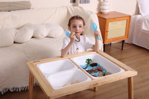 A child is eagerly engaging with the Sensory Table, complete with one large bin and a Dinosaur Sensory Bin Sand Toys Set, featuring sand, rocks, and sensory dinosaur toys alongside animal figures near a cozy sofa in the living room.