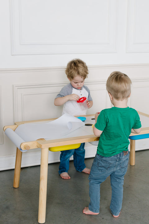 Two young children stand at the Painting Art Sensory Table with Paper Roll & Paint Cups + Bins, actively participating in a craft activity.