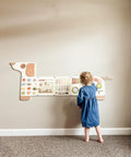 A child in a blue dress investigates the Dog Activity Wall Busy Board Panel, engaging with the sensory wall toy in a carpeted room with a beige backdrop.